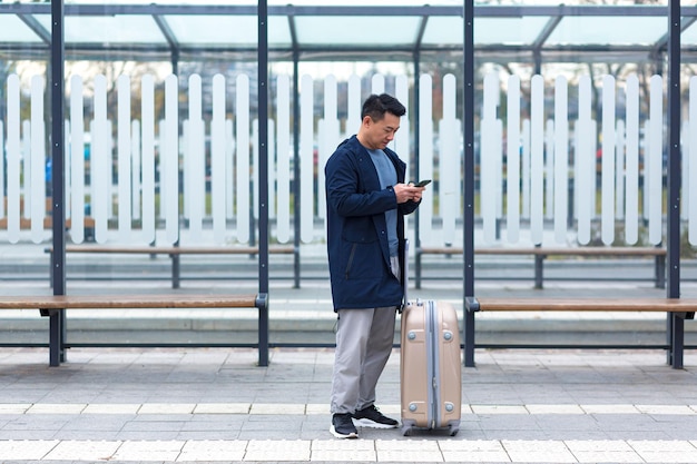Un touriste chinois senior utilise une application de téléphonie mobile pour réserver un hébergement et appeler un taxi, un homme près de l'aéroport avec une valise