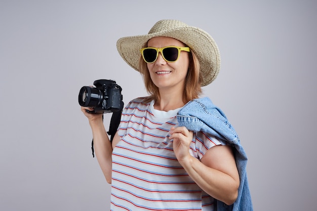 Photo une touriste dans un chapeau utilise un appareil photo, prend une photo. isoler sur fond gris.