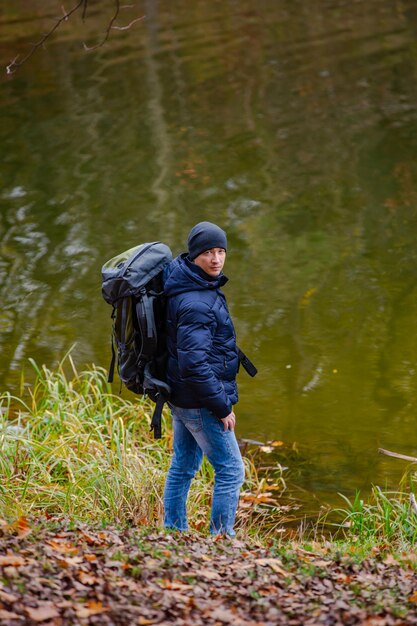 Touriste dans une veste et un jean regarde la caméra près de la rivière Fond de paysage d'automne