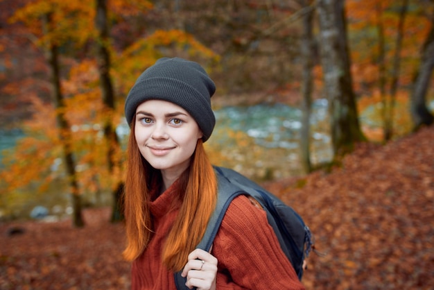 Une touriste énergique avec un sac à dos dans un pull rouge et des casquettes se repose dans la forêt d'automne du parc