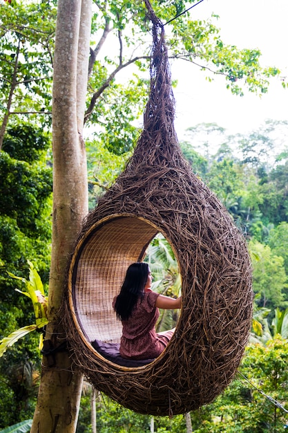 Une touriste est assise sur un nid de gros oiseau sur un arbre de l'île de Bali