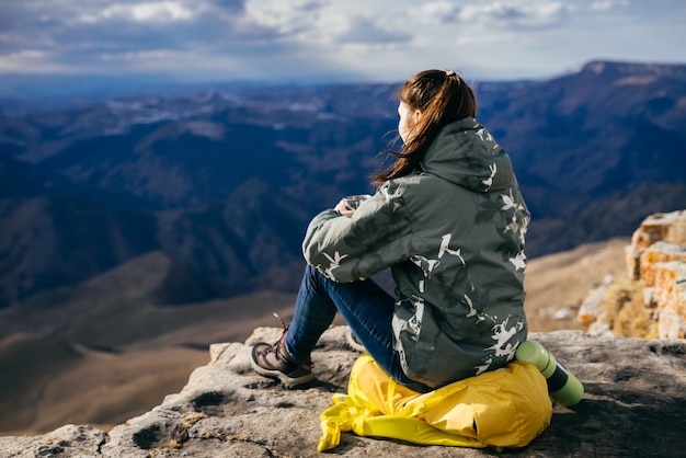 Une touriste est assise sur un sac à dos à l'arrière-plan des hautes montagnes