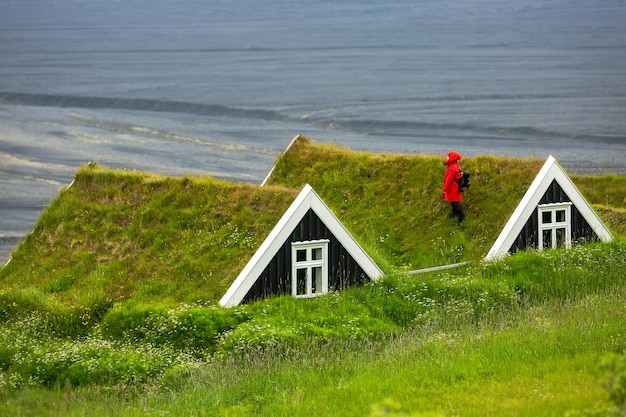 Touriste femelle dans une veste rouge se dresse sur le toit d'une maison de tourbe traditionnelle islandaise