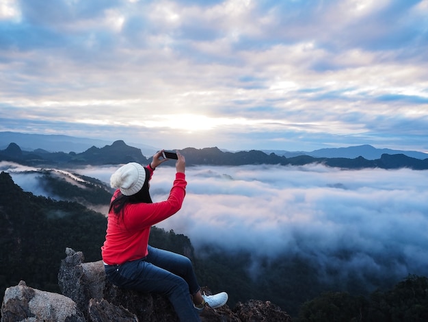 Touriste femme asiatique assis sur le rocher au sommet de la montagne et prendre la photographie du ciel du lever du soleil.