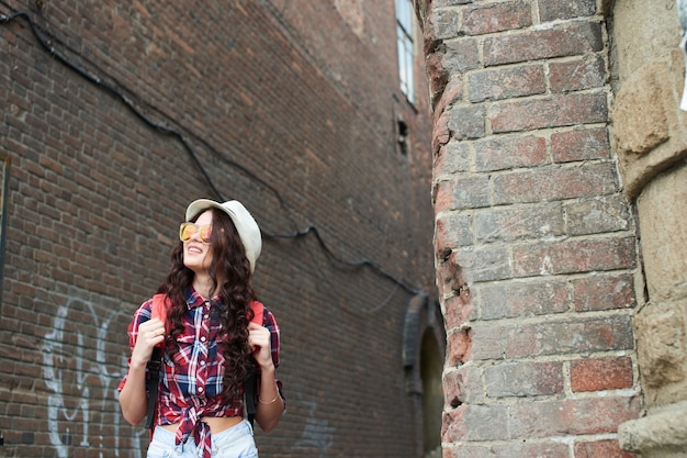 La touriste de fille avec le chapeau et les lunettes de soleil dans l'arrière de ruelle de brique rouge