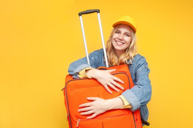 Une touriste heureuse embrasse une valise et sourit sur un concept de voyage de fond isolé jaune