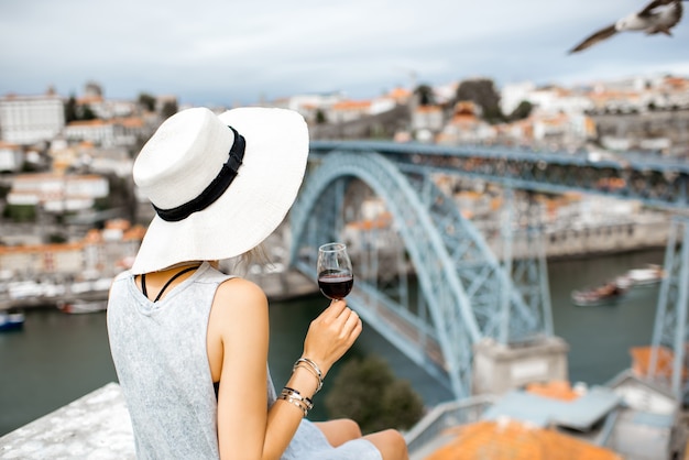 Touriste de jeune femme s'asseyant avec le verre de vin de Porto sur la terrasse avec la vue superbe de paysage urbain sur la ville de Porto au Portugal