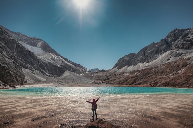 Le touriste lève la main avec un lac turquoise et une chaîne de montagnes au sommet