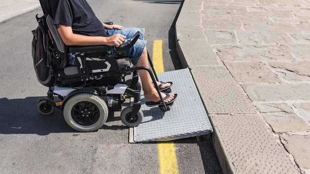 Photo touriste masculin en fauteuil roulant traversant la rampe du seuil sur la promenade balnéaire handicapée et