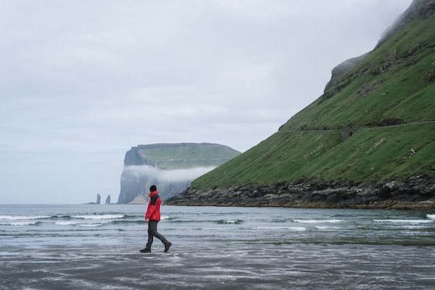 Touriste sur la plage dans le village de Tjornuvik, îles Féroé. Vue sur les cheminées marines de Risin et Kellingin