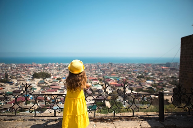 Une touriste portant un chapeau jaune et une robe d'été regarde d'une hauteur sur la terrasse d'observation de la ville Visite guidée L'enfant s'est perdu à la recherche de ses parents