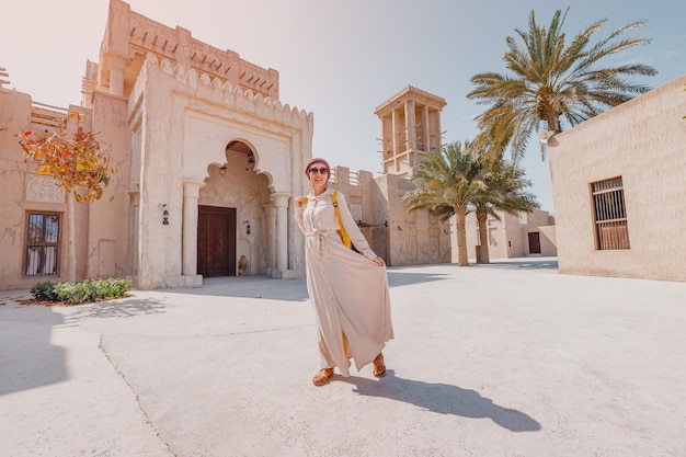 Une touriste portant un turban rouge et une robe longue beige se promène dans les vieilles rues étroites de Bur Dubai et du concept de voyage et de tourisme Creek