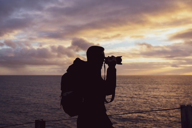 Touriste prenant une photo sur les falaises de Boca do Inferno au coucher du soleil