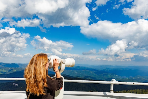 Une touriste regarde les paysages des Rhodopes et le ciel nuageux à travers le télescope sur la haute tour au sommet de Snezhan