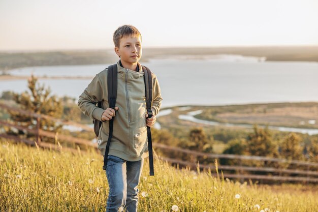 Touriste avec sac à dos debout au sommet d'une colline dans un champ d'herbe et profitant d'une belle vue sur le paysage Randonneur adolescent se reposant dans la nature Mode de vie actif Concept de voyage local