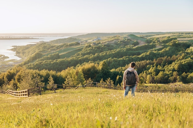 Touriste avec sac à dos debout au sommet d'une colline dans un champ d'herbe et profitant d'une belle vue sur le paysage Vue arrière d'un randonneur adolescent se reposant dans la nature Mode de vie actif Concept de voyage local