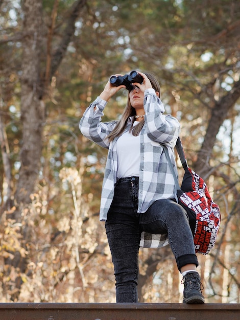 Une touriste se promène dans la forêt d'automne en regardant à travers des jumelles