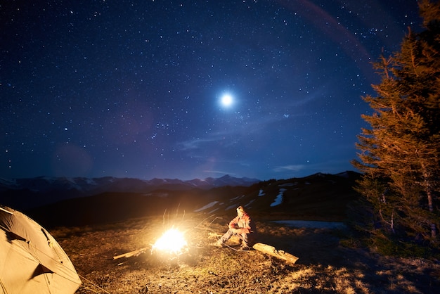 touriste se reposer dans son camp la nuit près d'un feu de camp