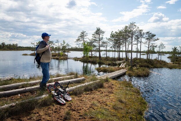 Photo un touriste se tient près d'un lac parmi une tourbière surélevée à proximité il y a des appareils pour marcher dans le marais