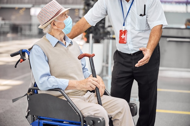 Touriste senior avec une canne à la main écoutant attentivement un employé de l'aéroport