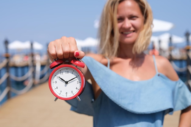 Une touriste souriante tenant un réveil sur la jetée de la mer