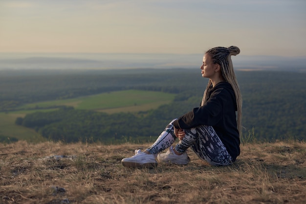 Une touriste sportive est assise sur de l'herbe sèche au sommet d'une montagne et regarde au loin contre la...