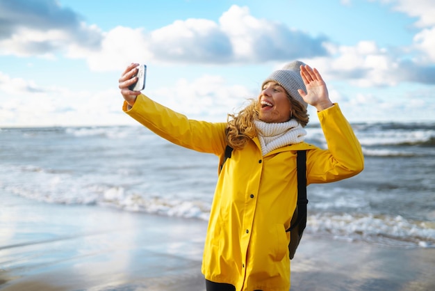 Touriste avec téléphone Selfie temps Touriste en veste jaune posant par la mer au coucher du soleil Voyage