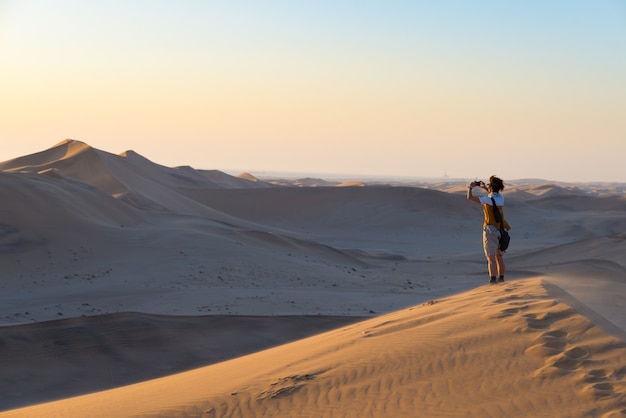 Touriste tenant un téléphone intelligent et prenant des photos à des dunes de sable pittoresques illuminés