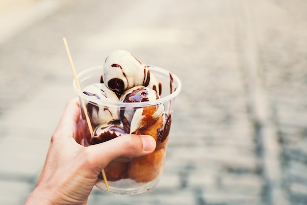 Le touriste tient dans la main des boules de beignets Fritule avec du chocolat sur fond de rues de Croatie