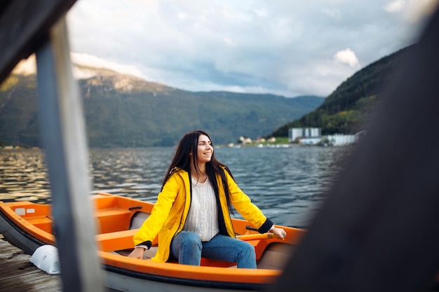 Une touriste en veste jaune est assise et pose dans un bateau sur fond de montagnes