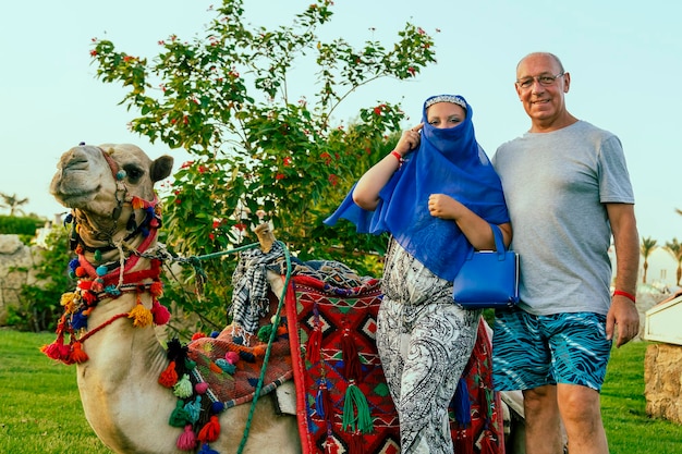 Touristes de couple de famille à côté de la femme de chameau couchée décorée avec le visage fermé de cap. photo horizontale