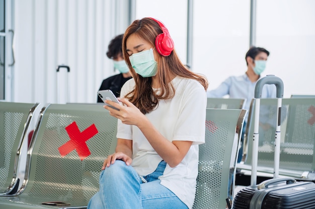 Les touristes féminines écoutent de la musique et portent des masques pour prévenir le virus en attendant de monter à bord de l'avion