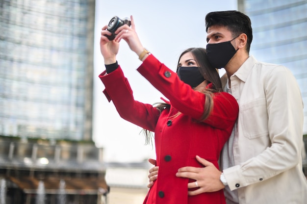 Des touristes heureux avec des masques de covid ou de coronavirus se battent ensemble dans une ville et photographient un endroit intéressant