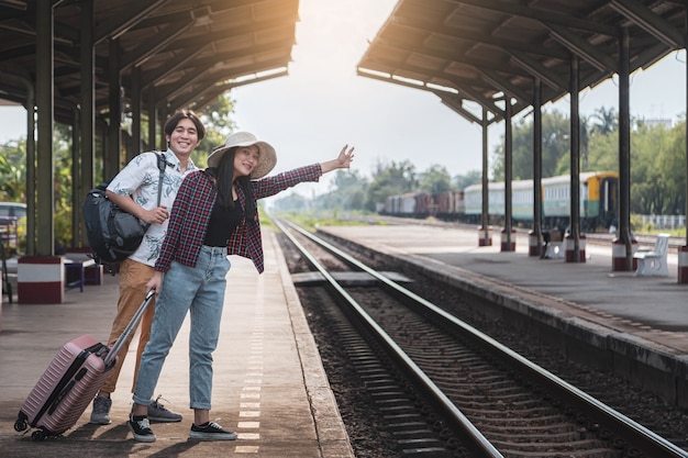 Les touristes masculins et féminins agitent leurs mains en attendant le train à la gare.