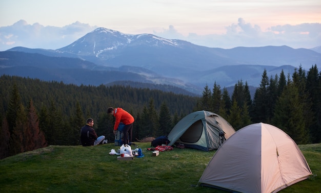 Les touristes masculins et féminins dans le camping près de deux tentes lors d'une randonnée avec leurs sacs à dos.