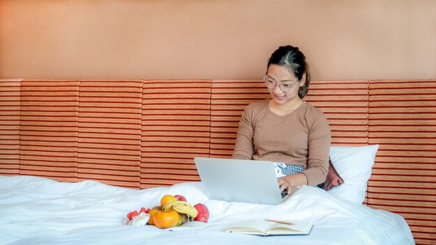 les touristes ont utilisé un ordinateur portable et ont mangé des fruits sur le lit dans le concept de nourriture saine de la chambre d'hôtel de luxe