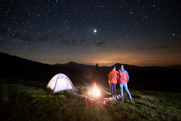 Touristes près de feu de camp et tente sous ciel étoilé de nuit