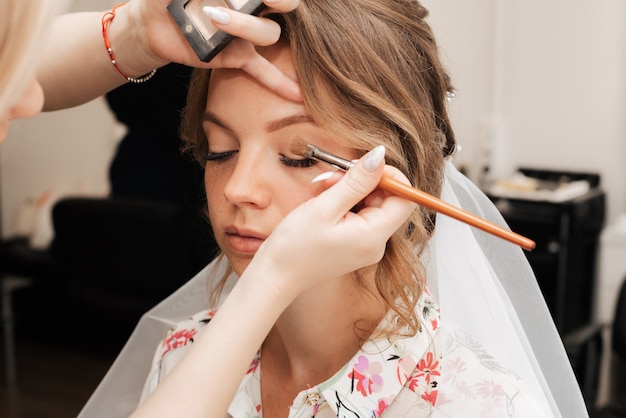 Tournage dans un salon de beauté. maquilleuse prépare la mariée avant le mariage le matin.