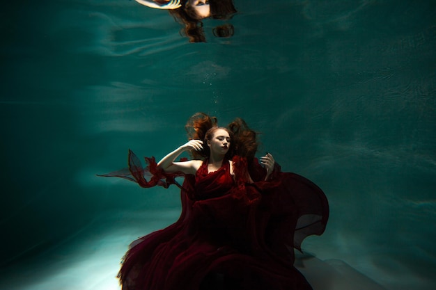 Le tournage sous-marin d'une belle jeune femme vêtue d'une robe rouge nage sous la surface de l'eau