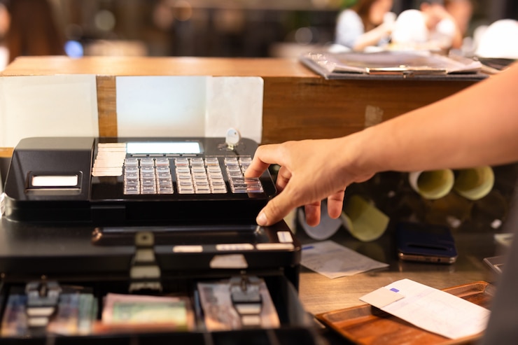 Photo tourné dans la main à faible lumière appuyant caisse enregistreuse électronique dans un magasin.