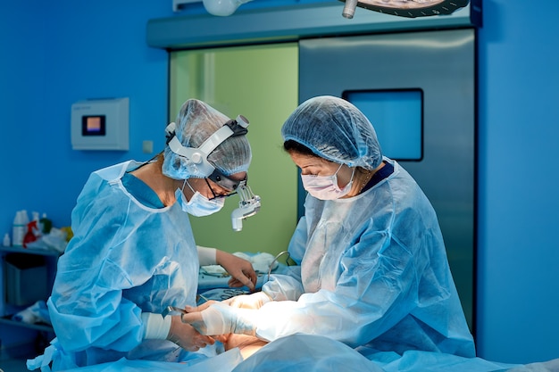 Tourné en salle d'opération, l'assistant distribue des instruments aux chirurgiens pendant l'opération. Les chirurgiens effectuent une opération. Médecins pratiquant la chirurgie.