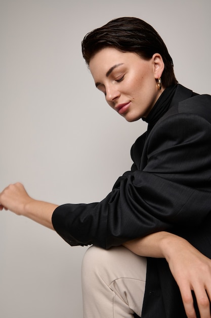 Tourné en studio de mode, portrait de la belle jeune femme européenne brune attrayante à la mode posant en regardant vers le bas assis aux trois quarts sur fond blanc avec espace de copie