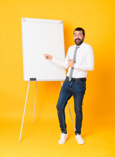 Tourné sur toute la longueur de l'homme d'affaires donnant une présentation sur tableau blanc sur jaune surpris et pointant le doigt sur le côté