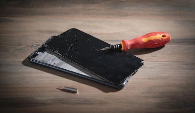 Tournevis et smartphone cassé sur la table en bois. Service de réparation