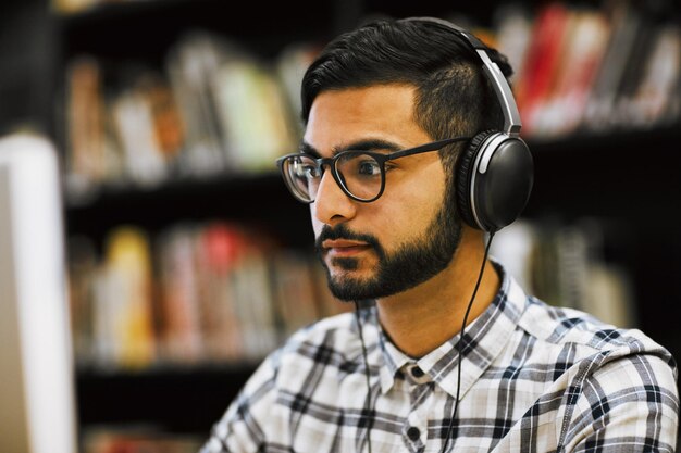 Tout cela va bientôt porter ses fruits Gros plan d'un jeune homme concentré assis et travaillant sur un ordinateur dans une bibliothèque tout en écoutant de la musique