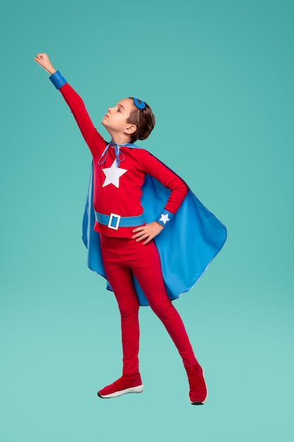 Photo tout le corps puissant garçon en costume de super-héros serrant le poing et se préparant à voler contre turquoise