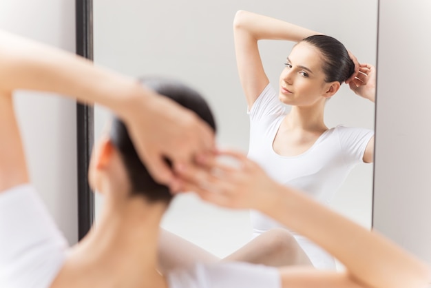 Tout doit être parfait. Belle jeune ballerine ajustant ses cheveux tout en étant assise contre un miroir et en regardant son reflet