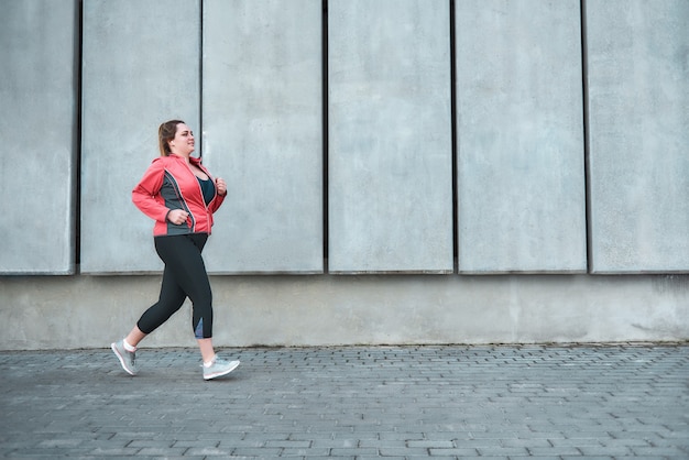 Tout est possible. Jeune femme de taille plus en vêtements de sport courir à l'extérieur. Mode de vie sain. Perte de poids. Notion de sport