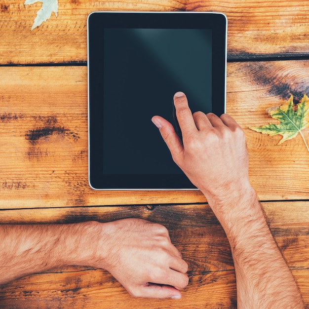 Tout le monde en une seule touche. Gros plan d'un homme tenant son doigt sur une tablette numérique alors qu'il était assis à la table en bois à l'extérieur