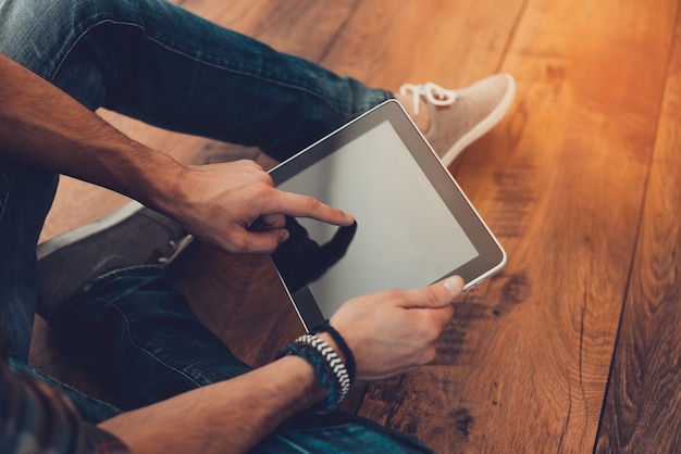 Tout le monde en une seule touche. Vue de dessus en gros plan de l'homme à l'aide d'une tablette numérique alors qu'il était assis sur le plancher en bois